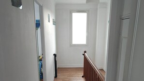 Ein schmaler Flur mit Holzboden, weißen Wänden und einem Fenster am Ende.