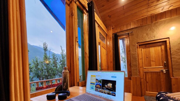 Una habitación de cabaña de madera con una computadora portátil sobre un escritorio, una ventana con vistas a las montañas y una puerta.