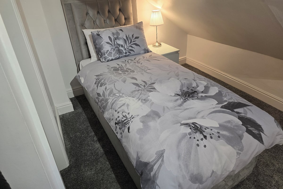 A neatly made bed with a floral bedspread, a tufted headboard, and a bedside lamp.