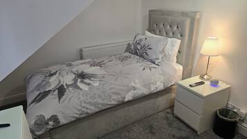 A bedroom with a bed, a nightstand, a lamp, and a trash can.