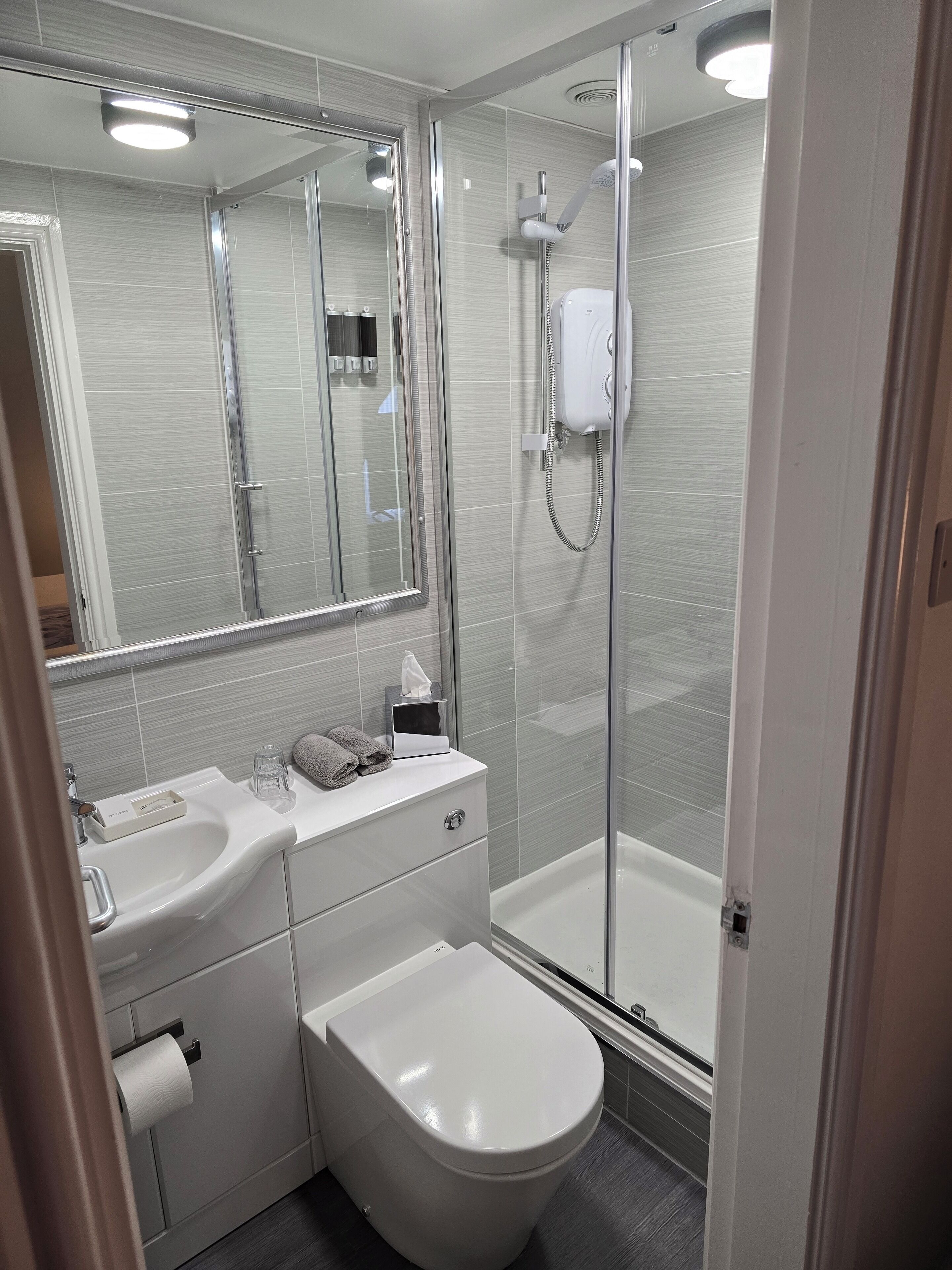 Et moderne badeværelse med et glasbadeværelsesafskærmning, en hvid vask og et toilet.