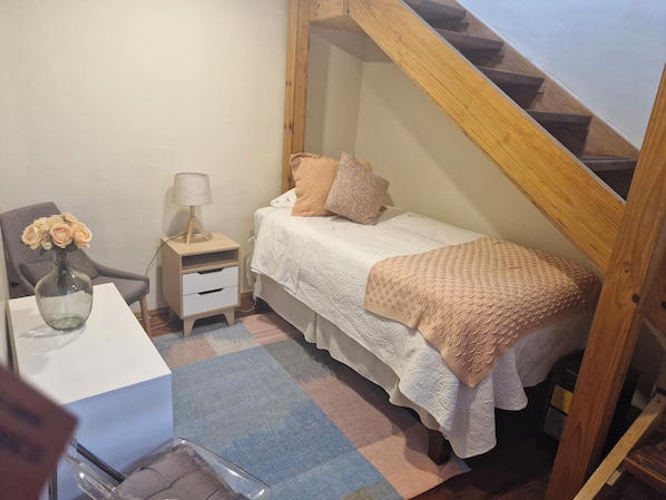 Un dormitorio con cama, mesita de noche, lámpara, silla y escritorio.