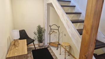 Une petite pièce chaleureuse, avec un plancher en bois, un tapis noir, une chaise, une petite table, une plante suspendue et un tabouret en bois.