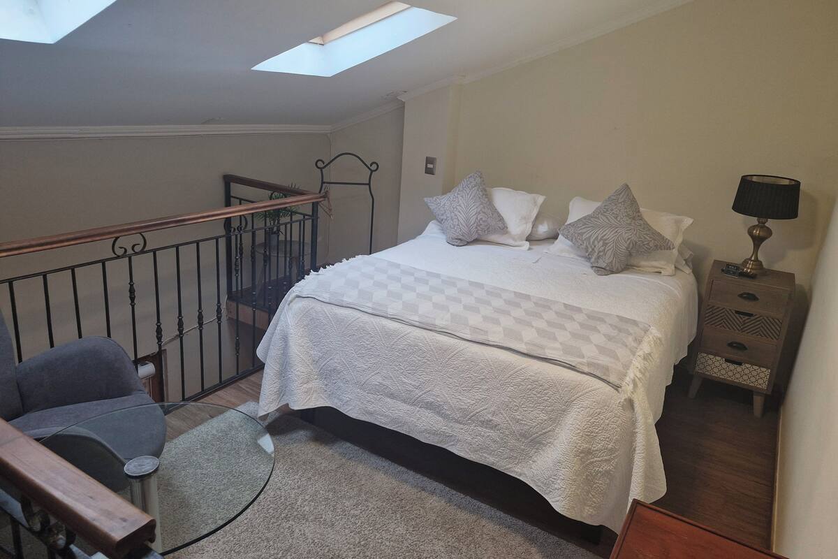 A bedroom with a bed, bedside table, lamp, and a view of a balcony.