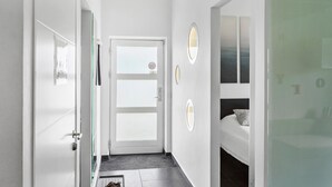 A narrow hallway with a door at the end, a bed with a pillow, and a wall with a mirror and a framed picture. - 3 bedroom amazing home in Rødby (Rødby)