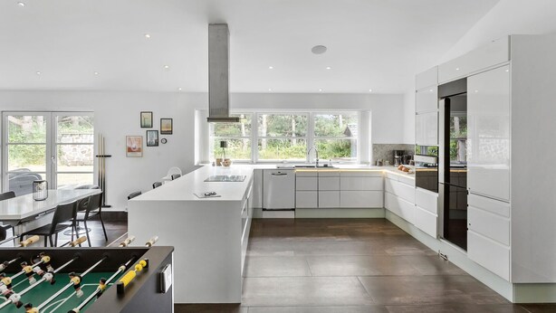 A modern kitchen with a central island, large windows, and a dining area with a foosball table. - 3 bedroom amazing home in Rødby (Rødby)