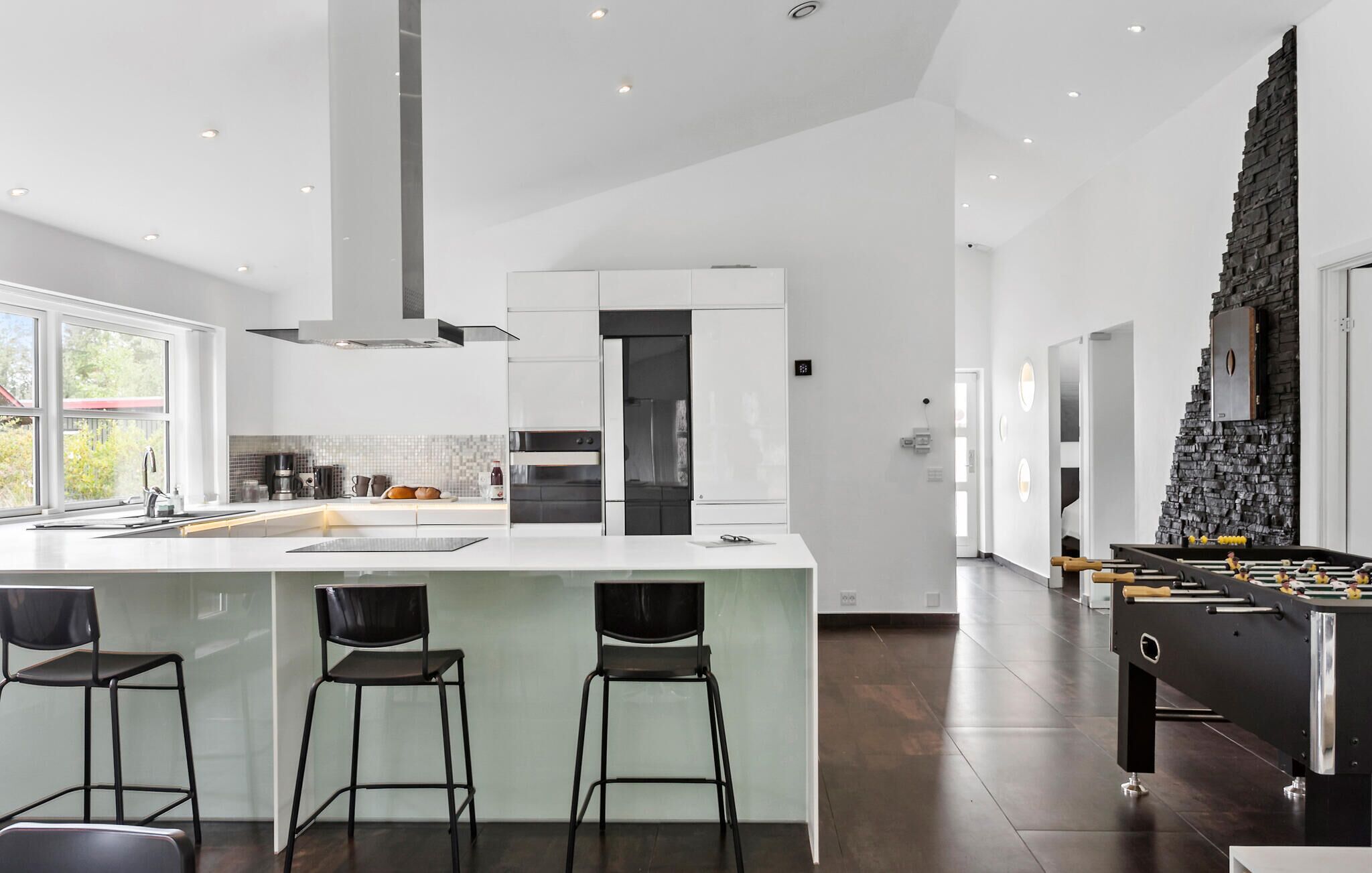 A modern kitchen with a large island, bar stools, and a stone accent wall.