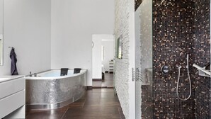 A modern bathroom with a freestanding bathtub, a shower area with mosaic tiles, and a visible hallway leading to another room. - 3 bedroom amazing home in Rødby (Rødby)