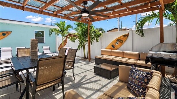 Un patio al aire libre con techo de madera, un ventilador de techo, una mesa de comedor con sillas, un sofá y una parrilla.