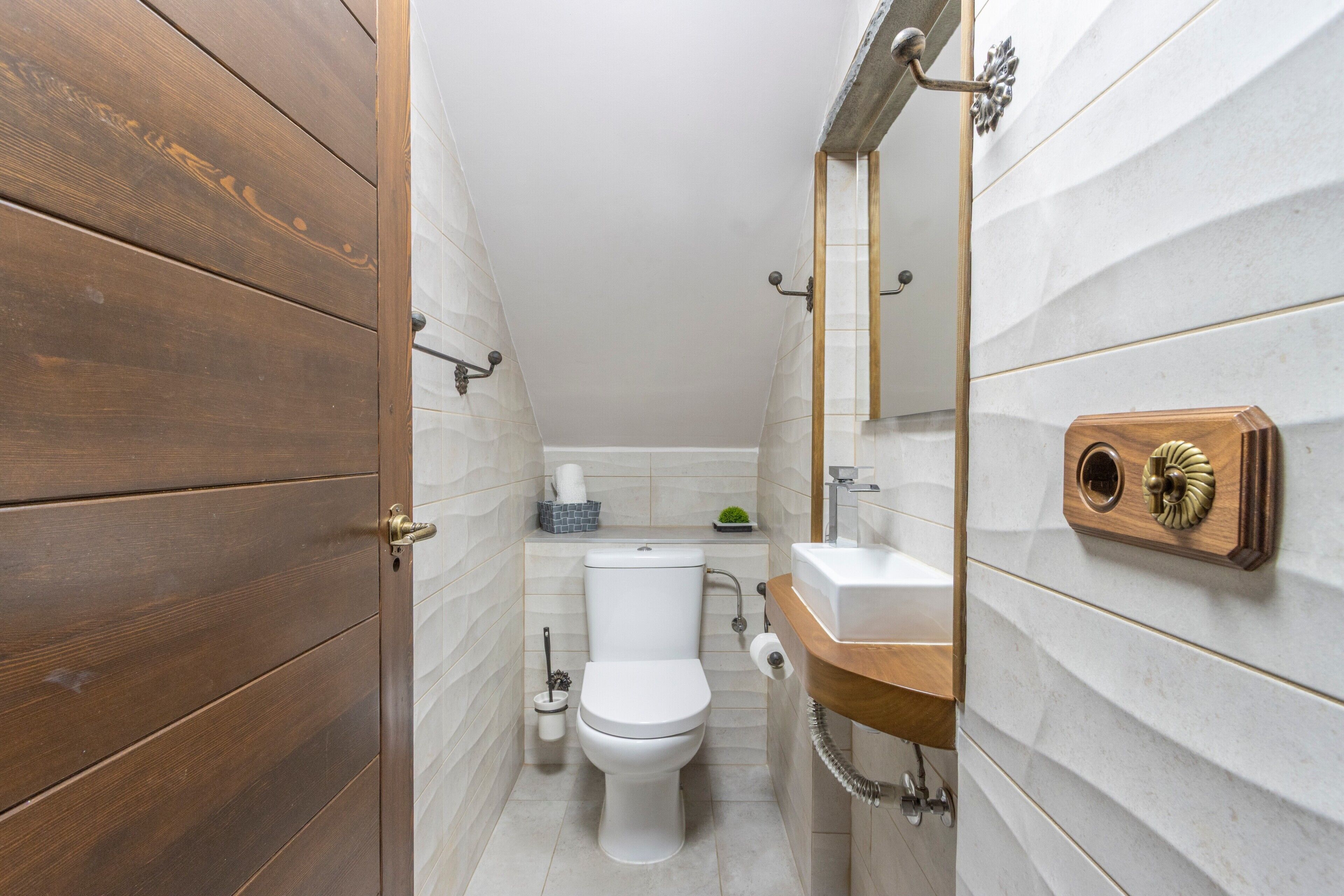 A bathroom with a wooden door, a toilet, a sink, and a mirror.