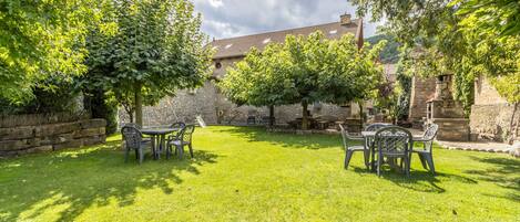 A courtyard with stone walls, two tables with chairs, and trees.