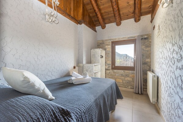 Un dormitorio con cama, radiador, ventana con cortinas y pared de piedra.
