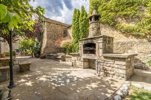Un patio de piedra con un horno de ladrillo tradicional, bancos de piedra y plantas en macetas.