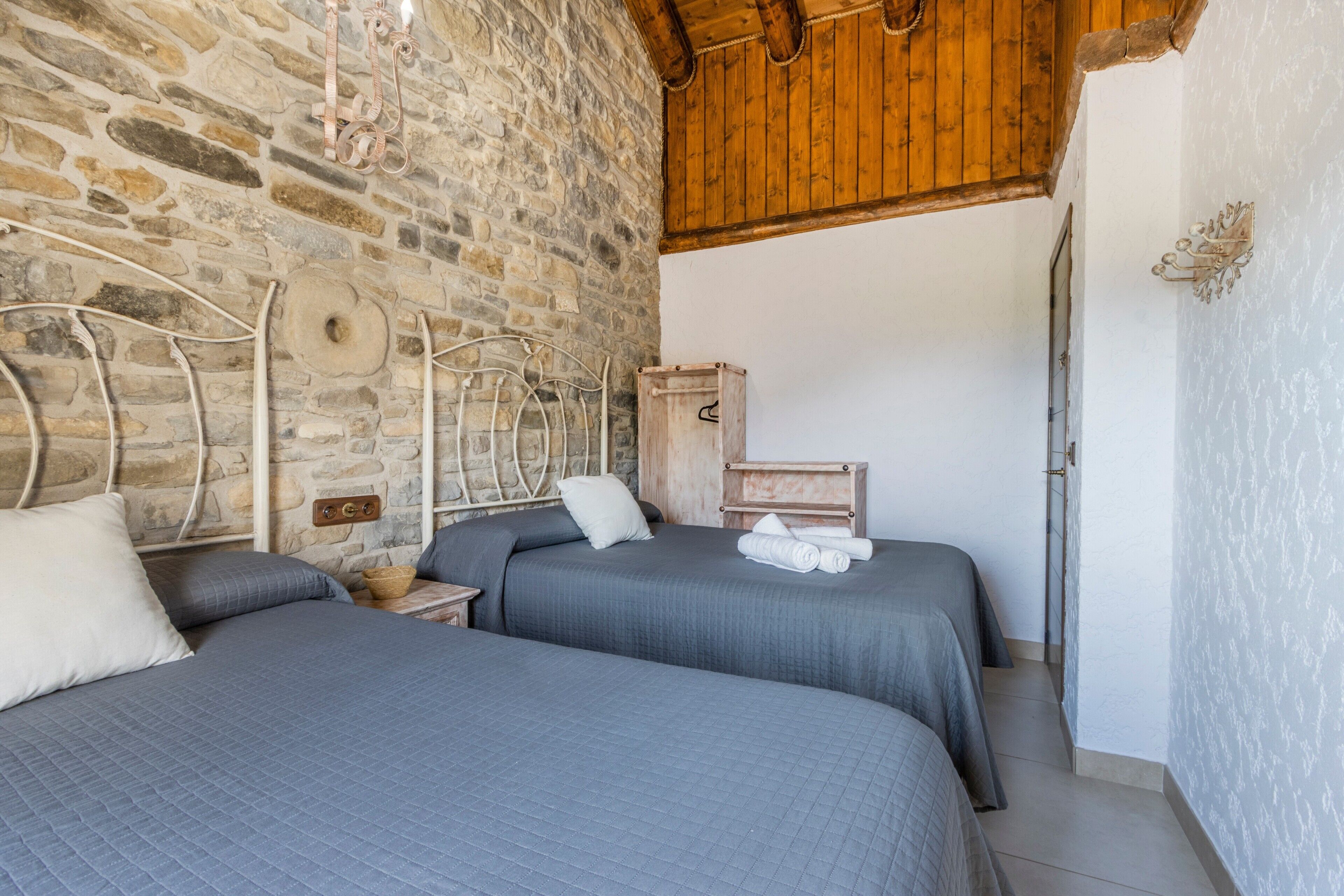 A bedroom with two beds, stone walls, wooden ceiling beams, and a white door.
