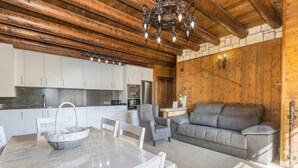 A wooden interior with a dining table, chairs, a grey sofa, and a kitchen area with cabinets and appliances. - Apartment 'Bachella' with Mountain View, Private Terrace and Wi-Fi (Borrastre)