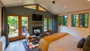Ein Schlafzimmer mit Bett, Fernseher, Kamin, Deckenventilator und großen Fenstern.