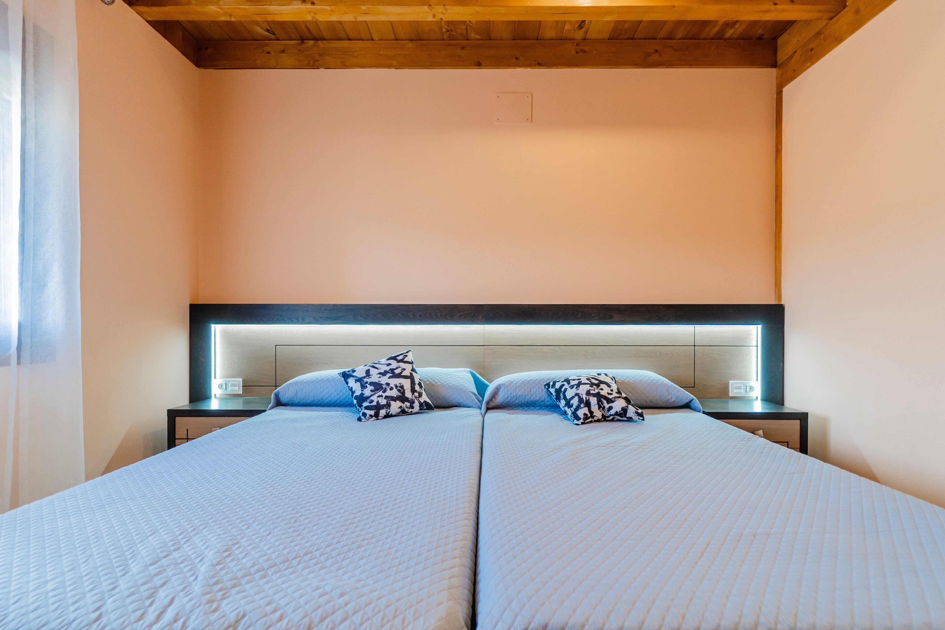 Una cama doble con cabecera, mesitas de noche y techo de madera.