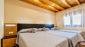 Ein Schlafzimmer mit zwei Betten, Holz-Kopfteilen, einer Holzkommode und einem Fenster mit transparenten Vorhängen.