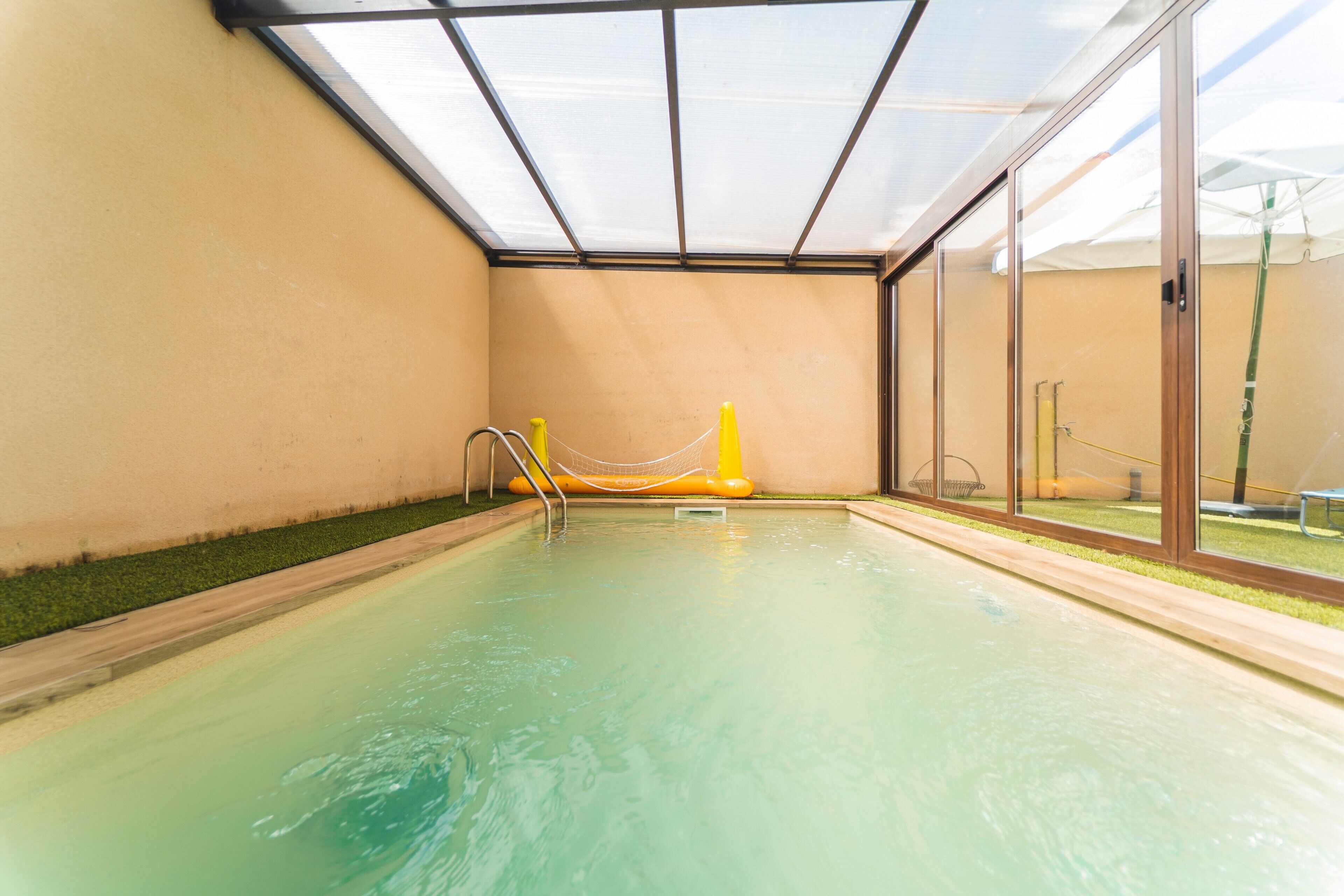 An indoor swimming pool with clear glass walls, a yellow safety rope, and a metal ladder.