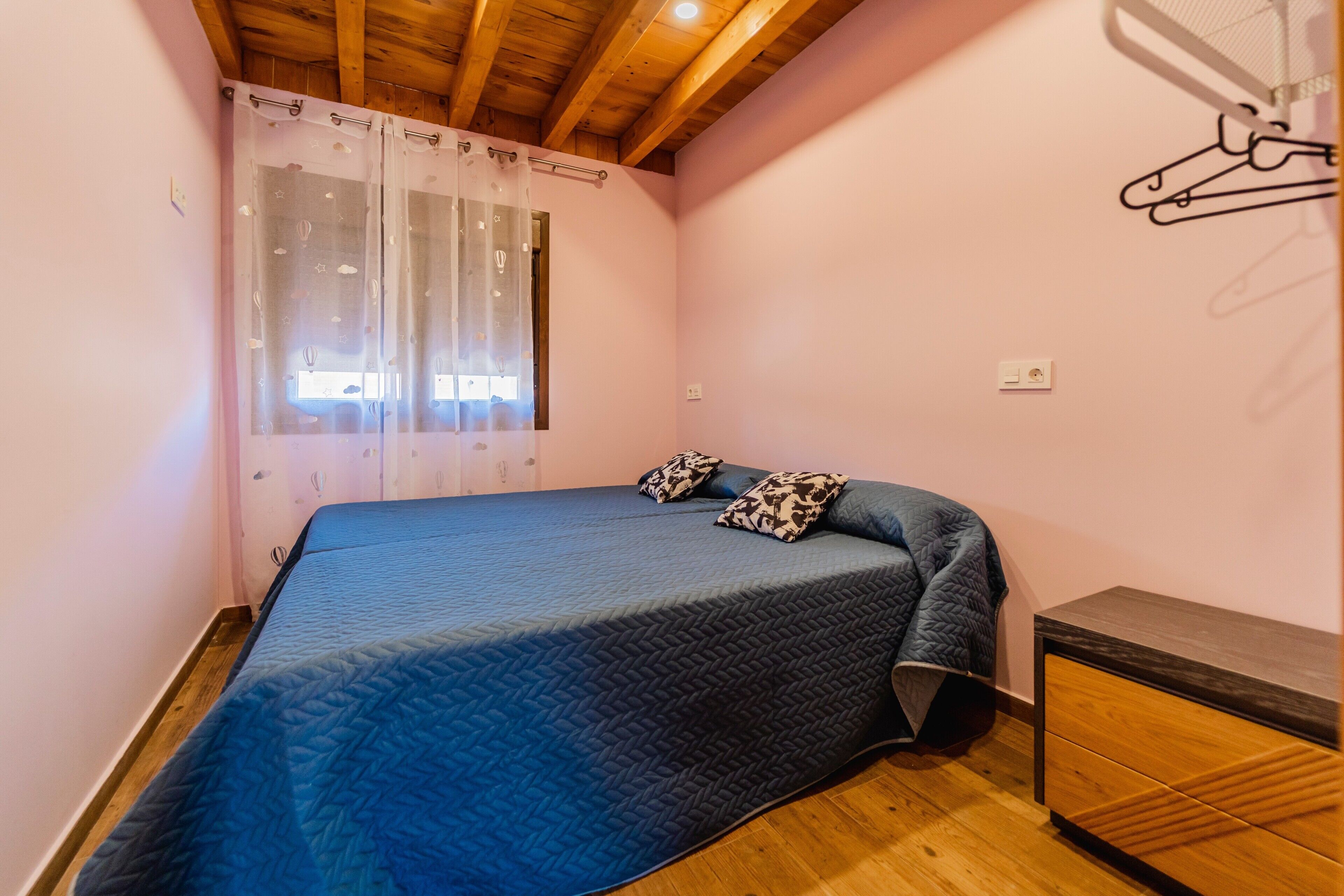 A bedroom with a bed, a window with curtains, a bedside table, and a wardrobe.
