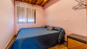 A bedroom with a bed, a window with curtains, a bedside table, and a wardrobe.