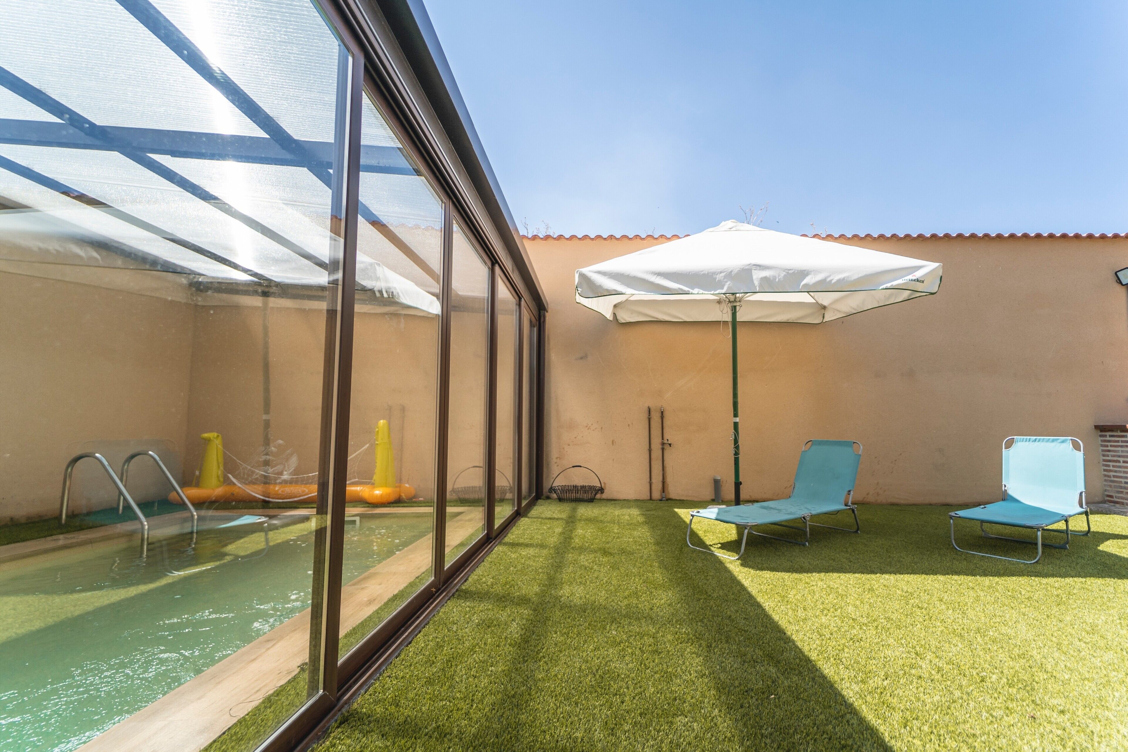 Een zwembadgedeelte met kunstgras, twee loungestoelen en een parasol.