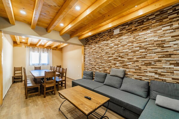 A wooden ceiling, a stone wall, a gray sofa, and a wooden dining table.