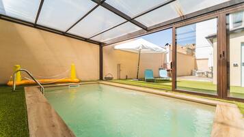 Una piscina interior con techo de vidrio, cubierta de madera y vistas al exterior.