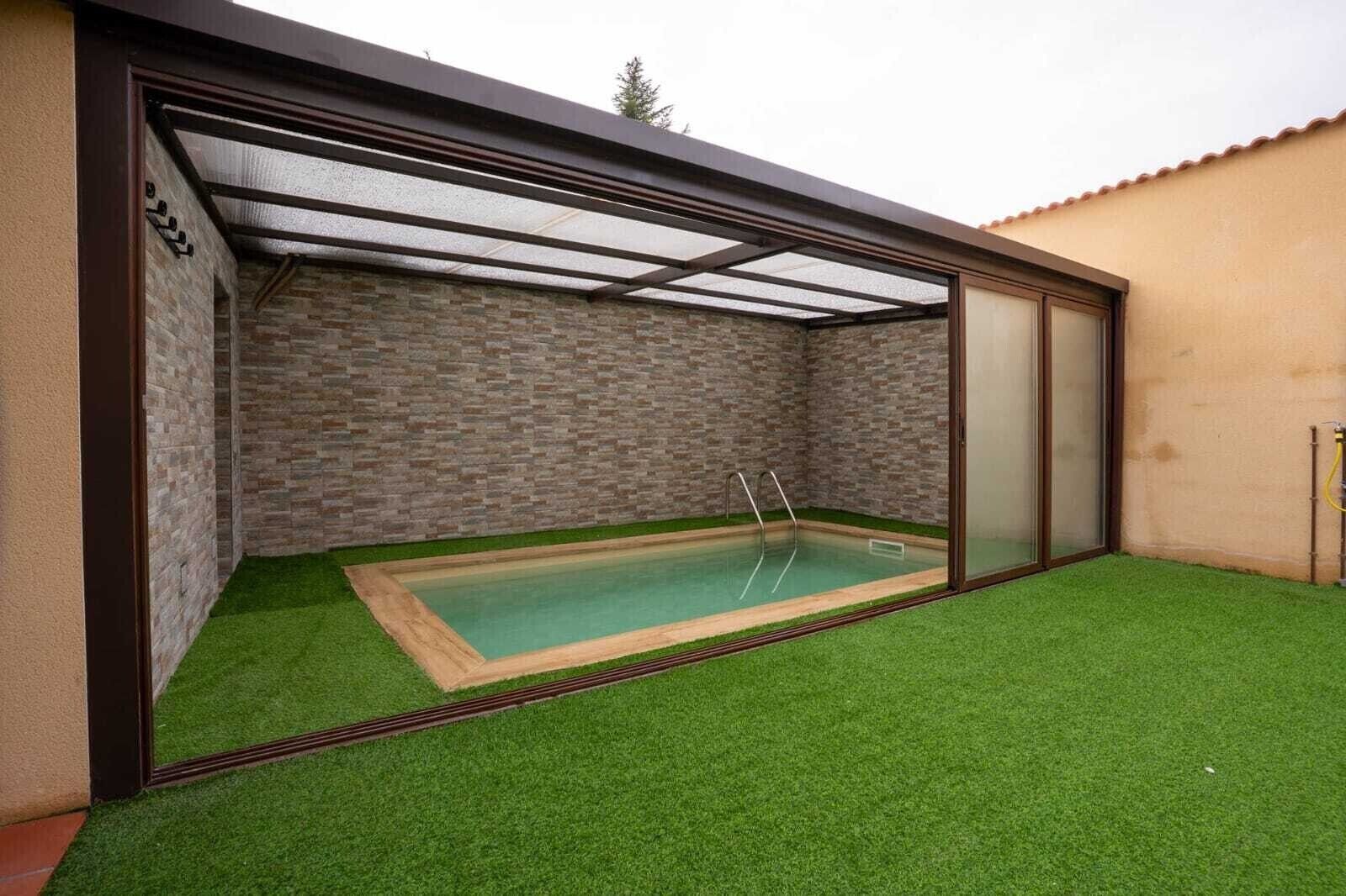 En swimmingpool med en glasvägg runt om, omgiven av konstgräs och en mur av tegelsten.