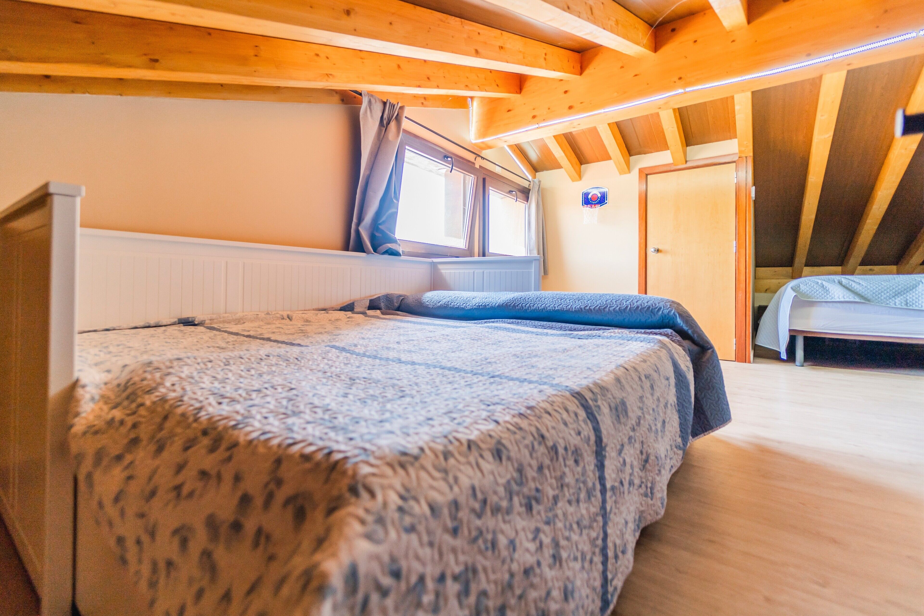 Un dormitorio con cama, ventana, puerta y vigas de madera en el techo.