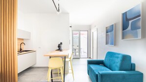 Une chambre moderne avec un coin cuisine, un canapé bleu, un fauteuil jaune et des œuvres d’art abstraites accrochées au mur.