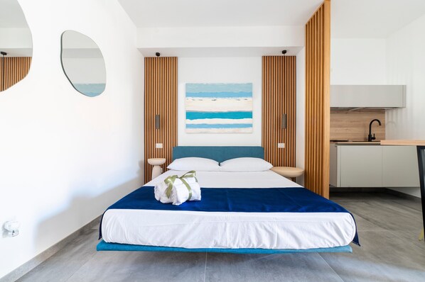 A modern hotel room with a bed, a desk, and a painting of a beach.