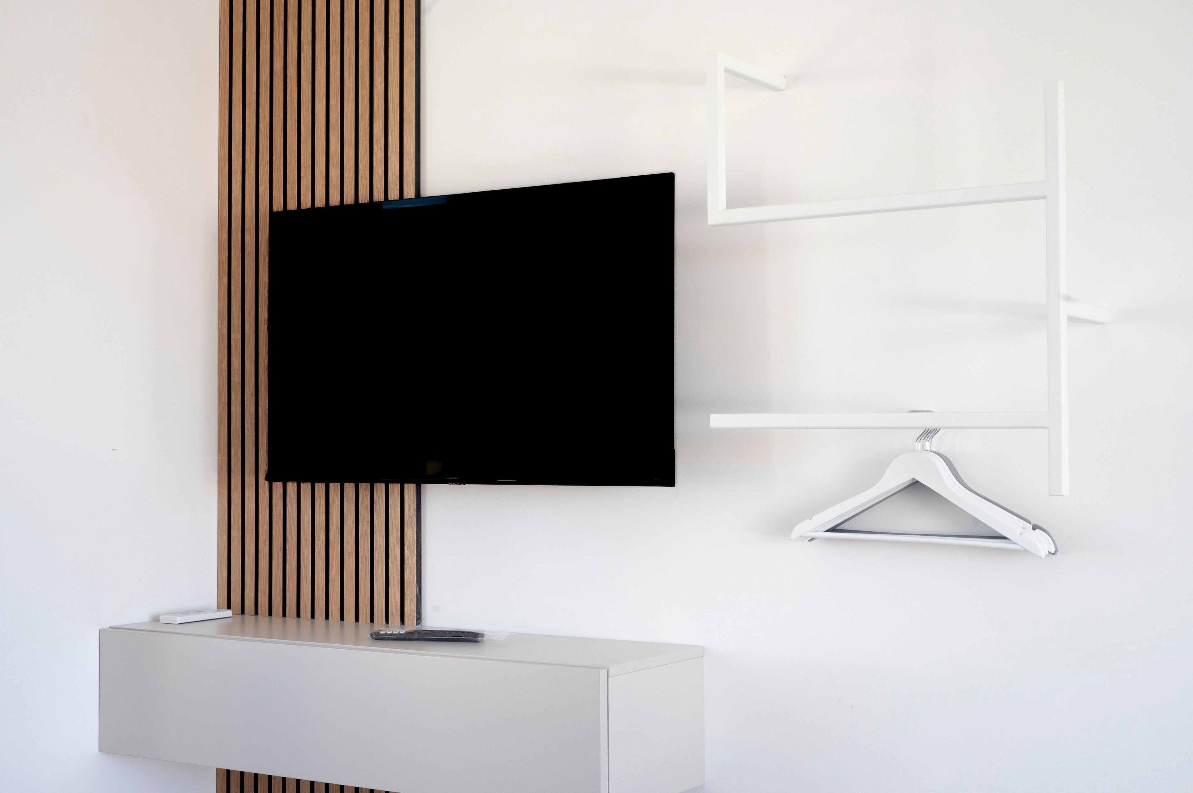 Una habitación moderna con televisor montado, una consola blanca y un panel de pared de madera.