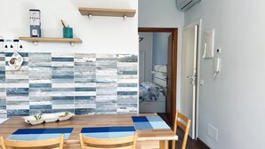A dining area with a wooden table, chairs, and a wall with a blue and white patterned backsplash. - S341 - Sirolo, new two-room apartment in the center with parking space (Sirolo)
