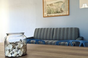 Una habitación con un sofá a rayas, una mesa de madera y un frasco de vidrio lleno de caracolas.