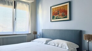 A bedroom with a bed, a radiator, a window with blinds, a wall-mounted painting, and a bedside lamp. - S340 - Sirolo, new two-room apartment in the center with parking space (Sirolo)