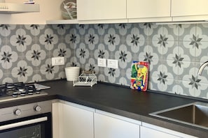 A kitchen with a gas stove, oven, white cabinets, a patterned backsplash, and a colorful children's book.