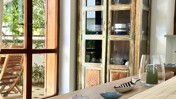 Ein Zimmer mit einem Holztisch, einer Vitrine und Blick auf Grün.