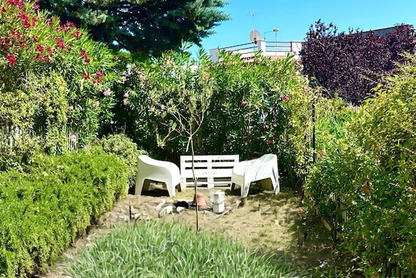 A garden with two white chairs, a wooden fence, and various plants.