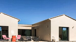 Ein Gebäude mit überdachter Terrasse, Sitzgelegenheiten im Freien und einem Fass.