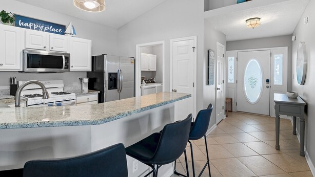 A modern kitchen with white cabinets, a granite countertop, and a bar area with black chairs.