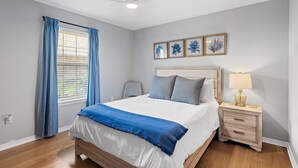 A bedroom with a bed, a nightstand with a lamp, a ceiling fan, and a window with curtains.