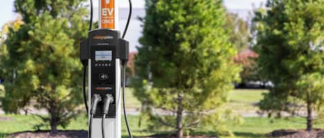 A charging station with a digital display, set against a backdrop of trees and grass.