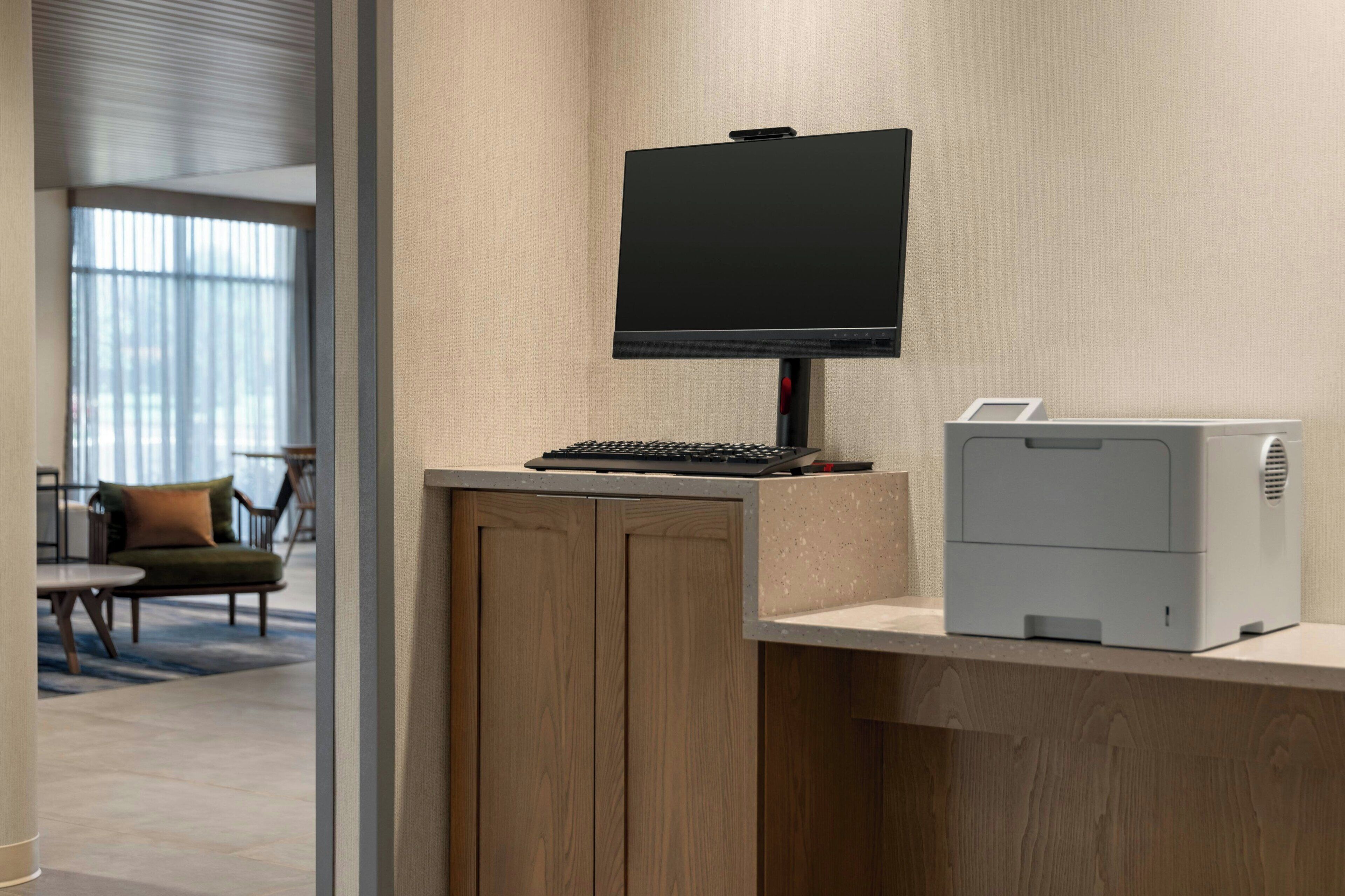 A reception desk with a flat-screen monitor, a keyboard, and a printer.