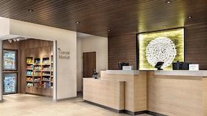 A hotel reception area with a wooden reception desk, a corner market with snacks, and a decorative wall piece. - Fairfield Inn & Suites by Marriott® Bethlehem Lehigh (Bethlehem)