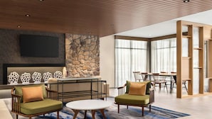 A modern living room with a stone accent wall, a flat-screen TV, and a dining area with a large window. - Fairfield Inn & Suites by Marriott® Bethlehem Lehigh (Bethlehem)