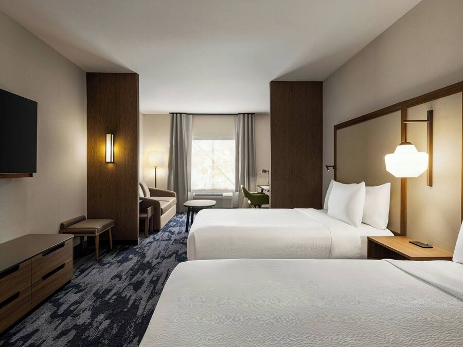 Habitación de hotel con dos camas, un escritorio, una silla, un televisor y una ventana con cortinas.