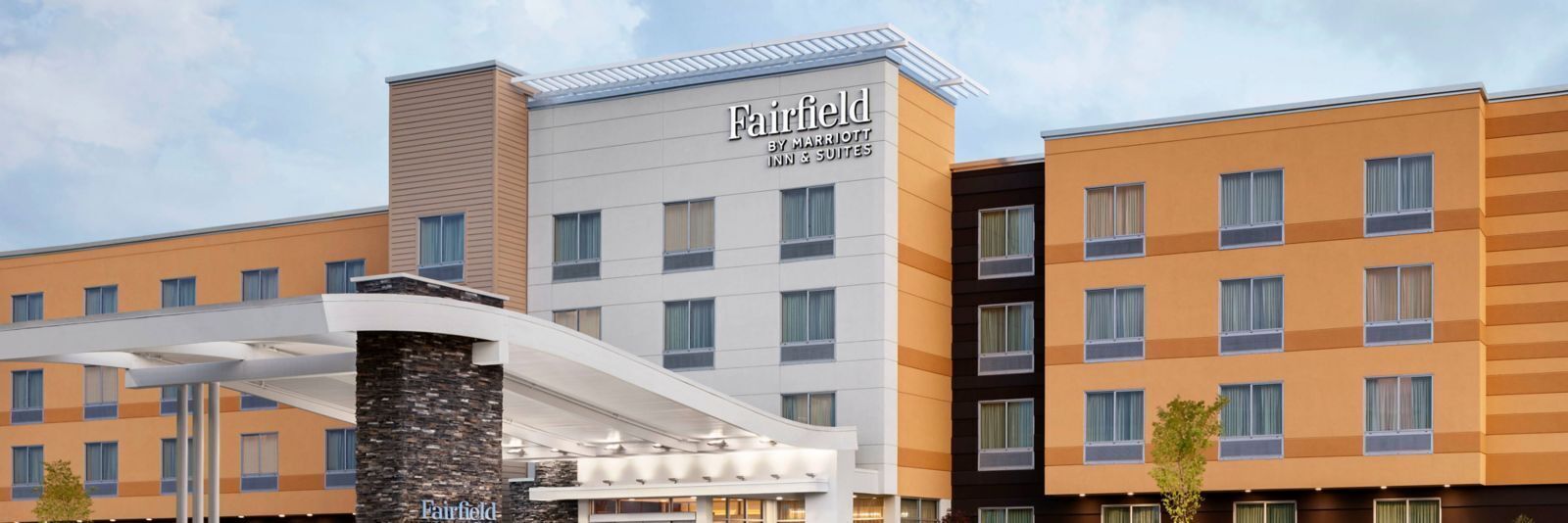 Um hotel Fairfield Inn & Suites com design moderno, destacando uma entrada imponente com galeria coberta e um pilar de pedra.