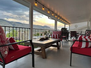 A covered outdoor seating area with red and white patterned cushions, a wooden table, and a grill. - The View on 87th Osoyoos 2 bedroom, 1.5 bath, covered patio view vacation home. (Osoyoos)