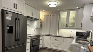 A modern kitchen with white cabinetry, stainless steel appliances, and a wooden floor. - The View on 87th Osoyoos 2 bedroom, 1.5 bath, covered patio view vacation home. (Osoyoos)